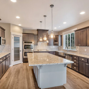 Design ideas for an expansive traditional u-shaped kitchen pantry in Seattle with a farmhouse sink, shaker cabinets, grey cabinets, granite benchtops, grey splashback, subway tile splashback, stainless steel appliances, with island and medium hardwood floors.