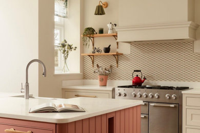 Large classic l-shaped kitchen/diner in London with a double-bowl sink, shaker cabinets, beige cabinets, engineered stone countertops, multi-coloured splashback, porcelain splashback, stainless steel appliances, porcelain flooring, an island, beige floors and white worktops.