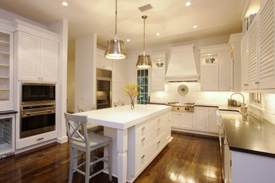 Mid-sized transitional u-shaped dark wood floor and brown floor enclosed kitchen photo in Tampa with a farmhouse sink, louvered cabinets, white cabinets, solid surface countertops, white backsplash, subway tile backsplash, stainless steel appliances, an island and black countertops