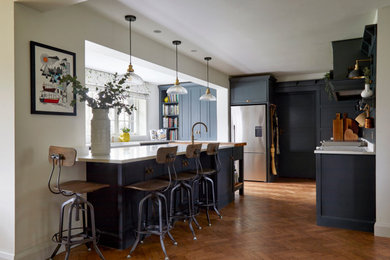 Example of a large classic medium tone wood floor and brown floor eat-in kitchen design in Hertfordshire with a double-bowl sink, shaker cabinets, green cabinets, quartzite countertops, white appliances, an island and white countertops