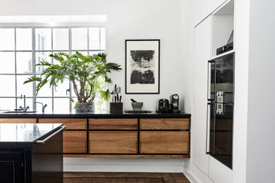 Inspiration for a large contemporary single-wall kitchen/diner in London with a built-in sink, flat-panel cabinets, dark wood cabinets, granite worktops, black appliances, dark hardwood flooring, an island and black worktops.