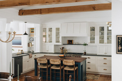 Inspiration for a timeless u-shaped medium tone wood floor, brown floor and exposed beam eat-in kitchen remodel in Grand Rapids with an undermount sink, glass-front cabinets, white cabinets, quartzite countertops, white backsplash, ceramic backsplash, stainless steel appliances, an island and black countertops