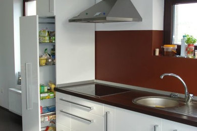 Cette image montre une grande cuisine américaine linéaire minimaliste avec un évier encastré, un placard à porte affleurante, des portes de placard blanches, un plan de travail en bois, une crédence marron, un électroménager en acier inoxydable, parquet foncé, aucun îlot et un sol marron.