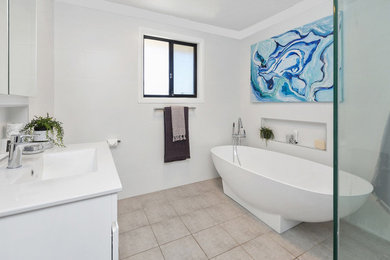 This is an example of a small contemporary bathroom in Sydney with raised-panel cabinets, a freestanding tub, white tile, ceramic tile, white walls, ceramic floors, a trough sink and solid surface benchtops.