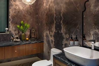 This is an example of a large contemporary powder room in Los Angeles with flat-panel cabinets, medium wood cabinets, a one-piece toilet, multi-coloured walls, cement tiles, a vessel sink, marble benchtops and grey floor.