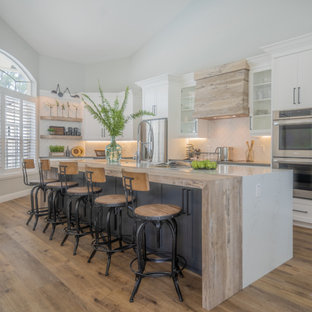 Large industrial open concept kitchen remodeling - Example of a large urban single-wall vinyl floor and beige floor open concept kitchen design in Miami with a farmhouse sink, shaker cabinets, white cabinets, quartzite countertops, white backsplash, subway tile backsplash, stainless steel appliances, an island and gray countertops
