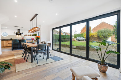 This is an example of a medium sized contemporary open plan dining room in Hertfordshire with white walls, light hardwood flooring, a two-sided fireplace, a brick fireplace surround and feature lighting.