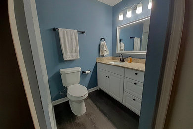 Example of a large white tile and ceramic tile vinyl floor, brown floor and single-sink bathroom design in Charlotte with a two-piece toilet, blue walls, an undermount sink, granite countertops and beige countertops