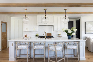 Open concept kitchen - coastal galley medium tone wood floor, brown floor and exposed beam open concept kitchen idea in Other with a farmhouse sink, shaker cabinets, white cabinets, white backsplash, stone slab backsplash, stainless steel appliances, an island and white countertops
