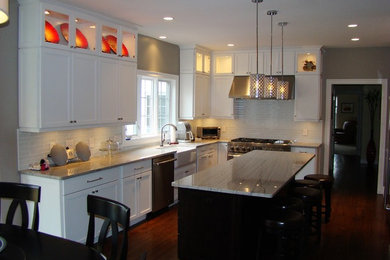 Photo of a large transitional l-shaped eat-in kitchen in New York with a farmhouse sink, shaker cabinets, white cabinets, granite benchtops, white splashback, porcelain splashback, stainless steel appliances, dark hardwood floors and with island.