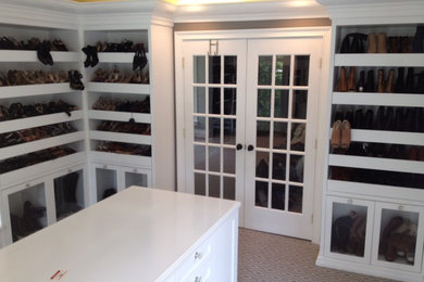 Large modern walk-in wardrobe for women in Philadelphia with glass-front cabinets, white cabinets and carpet.