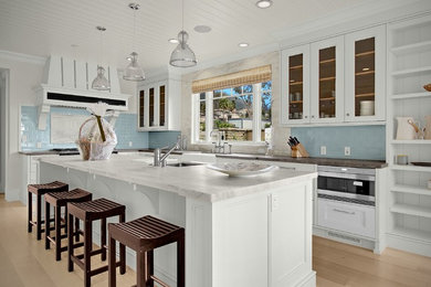 Large contemporary l-shaped eat-in kitchen in San Diego with a farmhouse sink, glass-front cabinets, white cabinets, marble benchtops, blue splashback, ceramic splashback, stainless steel appliances, light hardwood floors, with island, beige floor and white benchtop.