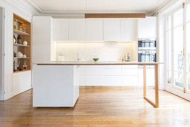 Inspiration for a large contemporary galley open plan kitchen in Paris with a single-bowl sink, flat-panel cabinets, white cabinets, white splashback, stainless steel appliances, light hardwood floors, with island, beige floor and white benchtop.