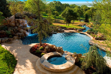 This is an example of a large country backyard custom-shaped natural pool in Oklahoma City with a hot tub and stamped concrete.