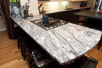 Example of a large country l-shaped medium tone wood floor kitchen design in Denver with a double-bowl sink, raised-panel cabinets, white cabinets, granite countertops, white backsplash, stone tile backsplash, stainless steel appliances and an island