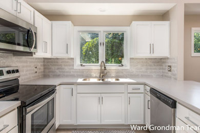 Example of a trendy u-shaped laminate floor and gray floor eat-in kitchen design in Grand Rapids with an undermount sink, shaker cabinets, white cabinets, quartzite countertops, beige backsplash, ceramic backsplash, stainless steel appliances, a peninsula and white countertops