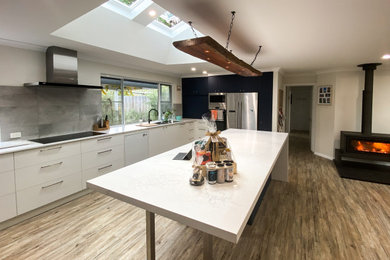 Large modern galley open plan kitchen in Other with a double-bowl sink, flat-panel cabinets, white cabinets, solid surface benchtops, grey splashback, porcelain splashback, stainless steel appliances, laminate floors, with island, beige floor and white benchtop.