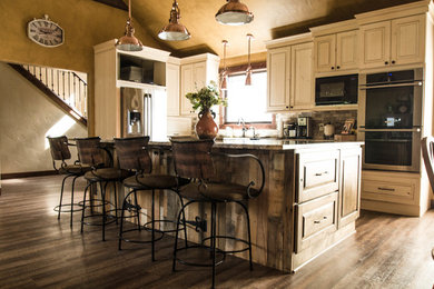 Farmhouse l-shaped brown floor eat-in kitchen photo in Other with a farmhouse sink, raised-panel cabinets, distressed cabinets, granite countertops, stainless steel appliances and an island