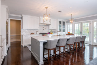 Eat-in kitchen - large traditional l-shaped brown floor eat-in kitchen idea in Philadelphia with shaker cabinets, white cabinets, white backsplash, an island, white countertops and stainless steel appliances