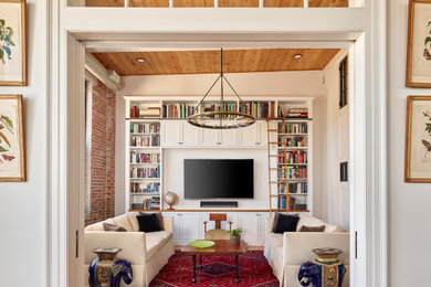 Cette image montre un salon mansardé ou avec mezzanine urbain de taille moyenne avec une bibliothèque ou un coin lecture, un mur blanc, un sol en bois brun, un téléviseur encastré, poutres apparentes et un mur en parement de brique.