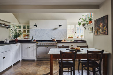 Inspiration for a traditional l-shaped kitchen/diner in Other with a belfast sink, shaker cabinets, white cabinets, grey splashback, stone slab splashback, stainless steel appliances, dark hardwood flooring, no island, brown floors and black worktops.