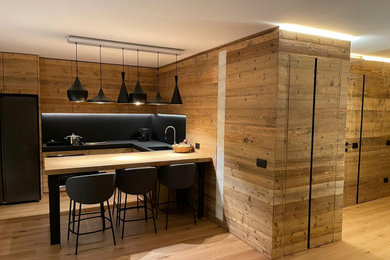 Imagen de cocina rústica con puertas de armario de madera clara, encimera de madera, salpicadero negro, suelo de madera clara, una isla y encimeras beige