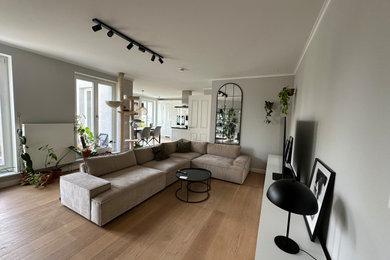 Großes, Offenes Skandinavisches Wohnzimmer mit grauer Wandfarbe, hellem Holzboden, Kamin, verputzter Kaminumrandung, freistehendem TV und beigem Boden in Hamburg
