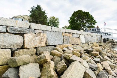 This is an example of a large coastal partial sun hillside stone retaining wall landscape in Other.