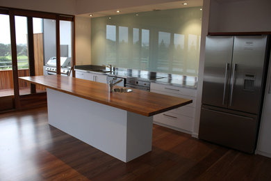 Inspiration for a modern galley kitchen pantry in Adelaide with an undermount sink, white cabinets, wood benchtops, green splashback, glass sheet splashback, stainless steel appliances, medium hardwood floors and with island.