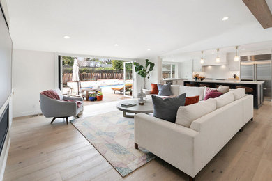 Example of a large minimalist open concept light wood floor, beige floor and exposed beam family room design in San Francisco with white walls, a ribbon fireplace, a metal fireplace and a wall-mounted tv