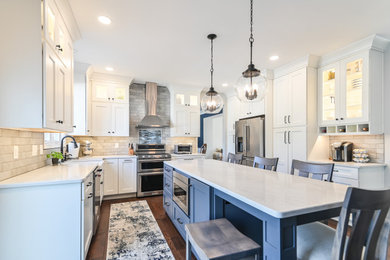 Kitchen - large transitional dark wood floor and brown floor kitchen idea in Philadelphia with a farmhouse sink, shaker cabinets, blue cabinets, quartz countertops, gray backsplash, subway tile backsplash, stainless steel appliances, an island and white countertops