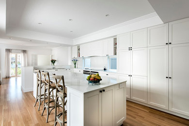 This is an example of a mid-sized country l-shaped open plan kitchen in Perth with a double-bowl sink, shaker cabinets, white cabinets, white splashback, light hardwood floors and with island.