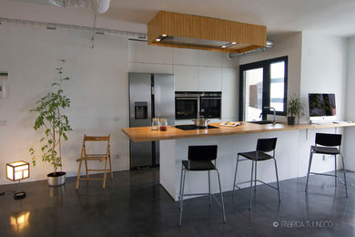 Exempel på ett industriellt linjärt kök med öppen planlösning, med en enkel diskho, släta luckor, vita skåp, träbänkskiva, rostfria vitvaror, betonggolv och en halv köksö