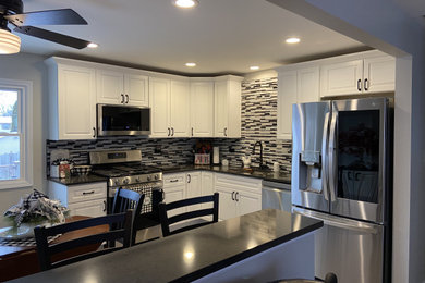 Example of a mid-sized minimalist l-shaped laminate floor and multicolored floor eat-in kitchen design in Chicago with an undermount sink, shaker cabinets, white cabinets, quartzite countertops, multicolored backsplash, glass tile backsplash, stainless steel appliances and black countertops