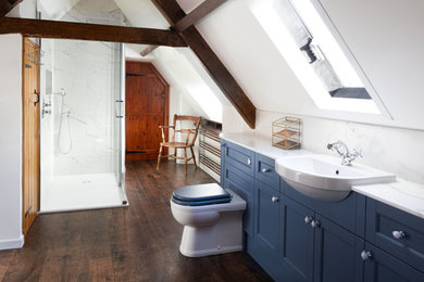 Inspiration for a large classic ensuite bathroom in Oxfordshire with recessed-panel cabinets, blue cabinets, a freestanding bath, a walk-in shower, a one-piece toilet, white tiles, porcelain tiles, white walls, vinyl flooring, a built-in sink, solid surface worktops, brown floors, a sliding door, white worktops, a wall niche, a single sink, a built in vanity unit and exposed beams.
