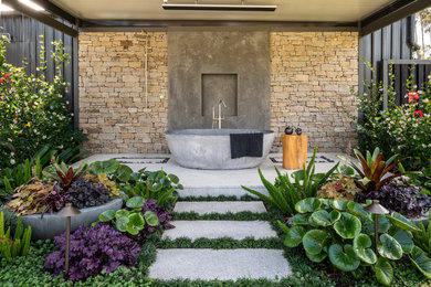 Large mediterranean backyard garden in Melbourne with natural stone pavers and a stone fence.