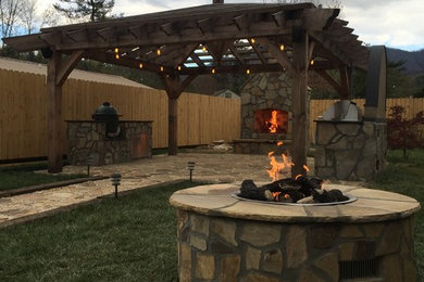 This is an example of a large transitional backyard patio in Other with a fire feature, natural stone pavers and a pergola.