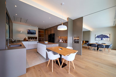 Photo of a large modern l-shaped open plan kitchen in Barcelona with an undermount sink, flat-panel cabinets, brown cabinets, marble benchtops, brown splashback, marble splashback, black appliances, porcelain floors, with island, beige floor and brown benchtop.