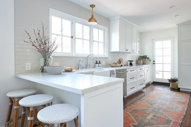 Inspiration for a mid-sized beach style galley eat-in kitchen in San Diego with an undermount sink, shaker cabinets, white cabinets, quartz benchtops, grey splashback, ceramic splashback, stainless steel appliances, medium hardwood floors, with island, brown floor and white benchtop.