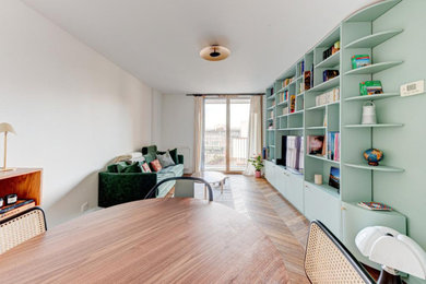 Ejemplo de sala de estar con biblioteca abierta moderna pequeña sin chimenea con paredes verdes, suelo de madera clara, pared multimedia, suelo beige y vigas vistas