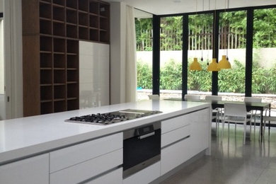 Eat-in kitchen - large modern single-wall ceramic tile eat-in kitchen idea with an undermount sink, flat-panel cabinets, white cabinets, quartz countertops, white backsplash, stone slab backsplash, stainless steel appliances and an island