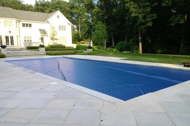 Imagen de piscina alargada clásica grande rectangular en patio trasero con adoquines de piedra natural