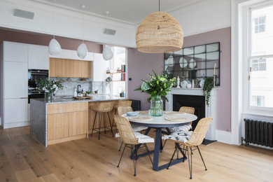 Photo of a large scandinavian kitchen/dining combo in Sussex with pink walls, light hardwood floors, a standard fireplace, a stone fireplace surround, brown floor and coffered.