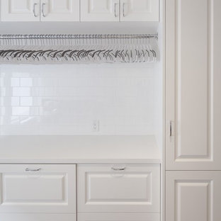 Immagine di una grande sala lavanderia classica con lavello sottopiano, ante con bugna sagomata, ante bianche, top in superficie solida, pavimento in laminato, lavatrice e asciugatrice affiancate, pavimento beige e pareti bianche