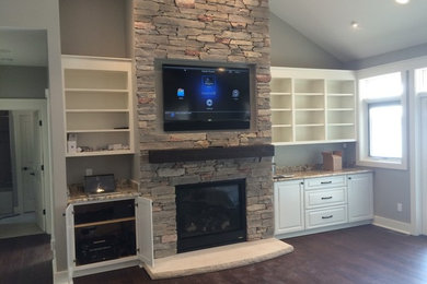 Inspiration for a mid-sized transitional enclosed dark wood floor and brown floor family room remodel in Other with gray walls, a standard fireplace, a stone fireplace and a wall-mounted tv