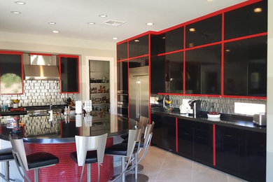 Kitchen - large eclectic l-shaped kitchen idea in Las Vegas with a farmhouse sink, stainless steel appliances, flat-panel cabinets, black cabinets, solid surface countertops, metallic backsplash, glass tile backsplash and an island