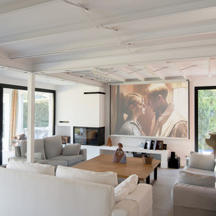 Ejemplo de salón abierto, mediterráneo, grande, con paredes blancas, suelo de baldosas de cerámica, chimenea de esquina, marco de chimenea de metal, pared multimedia y suelo gris