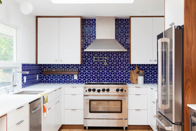 Design ideas for a midcentury kitchen in San Francisco with an undermount sink, flat-panel cabinets, white cabinets, quartz benchtops, blue splashback, ceramic splashback, stainless steel appliances, a peninsula, white benchtop and light hardwood floors.