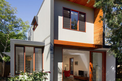 Photo of a midcentury two-storey grey house exterior in Melbourne with wood siding, a flat roof and a metal roof.