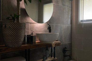 Photo of a mid-sized modern bathroom in Kansas City with medium wood cabinets, an alcove tub, a shower/bathtub combo, a two-piece toilet, gray tile, cement tile, beige walls, ceramic floors, a vessel sink, wood benchtops, a shower curtain, a single vanity and a built-in vanity.